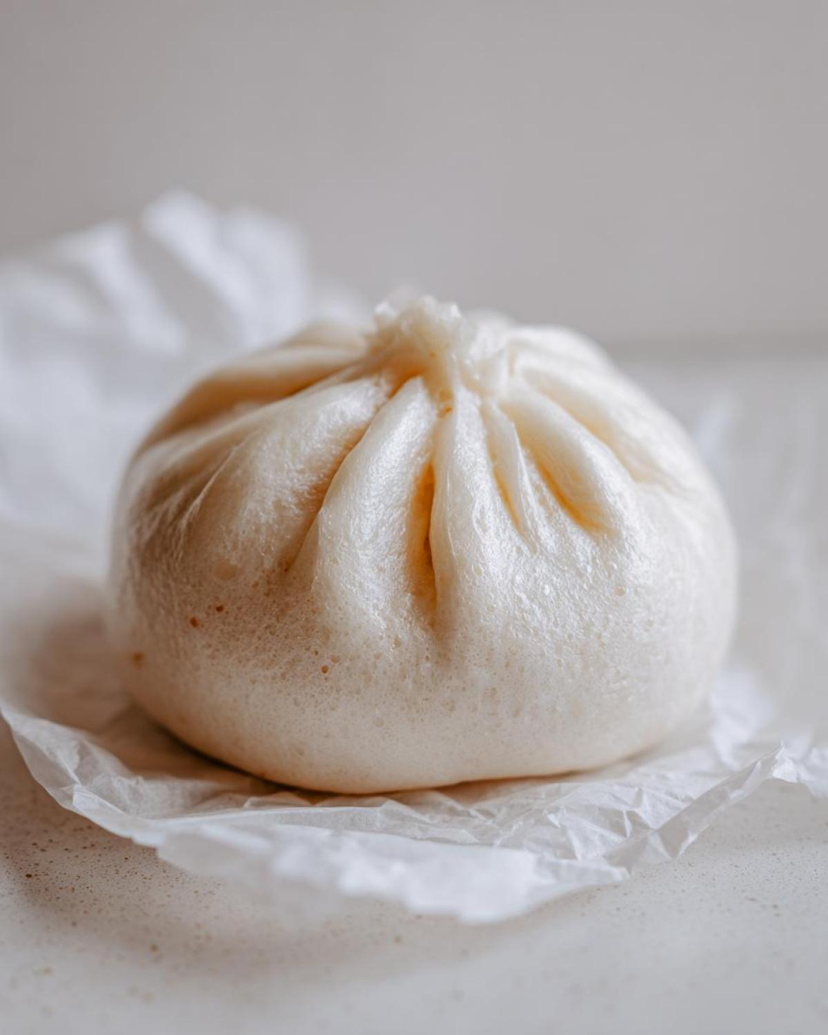 Close-up of a single, fluffy, steamed Char Siu Mushroom Bao resting on a piece of white parchment paper.