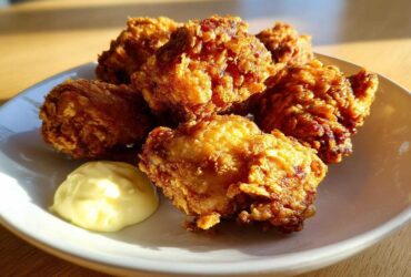 Five pieces of golden, crispy Chicken Karaage served on a white plate next to a dollop of Lemon Mayo.