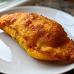 A single, golden-brown, battered and fried Chiles Rellenos Stuffed Poblanos resting on a white plate.