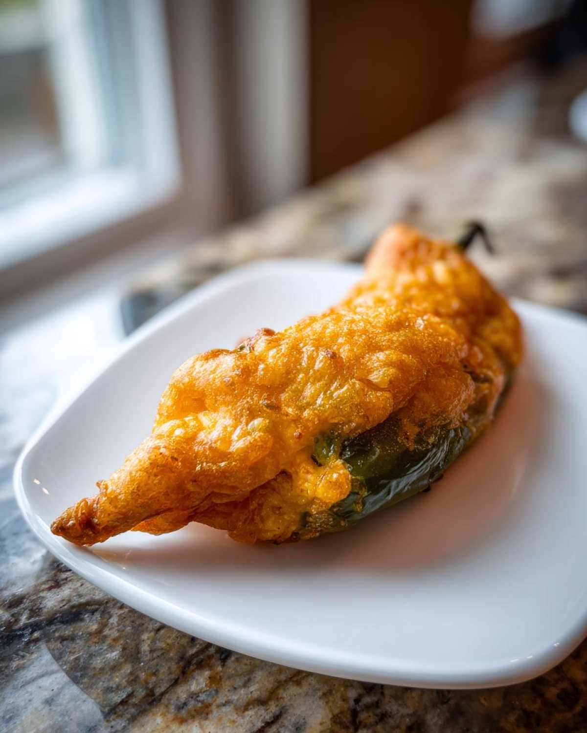 A single, golden-fried Chiles Rellenos Stuffed Poblanos resting on a white square plate.