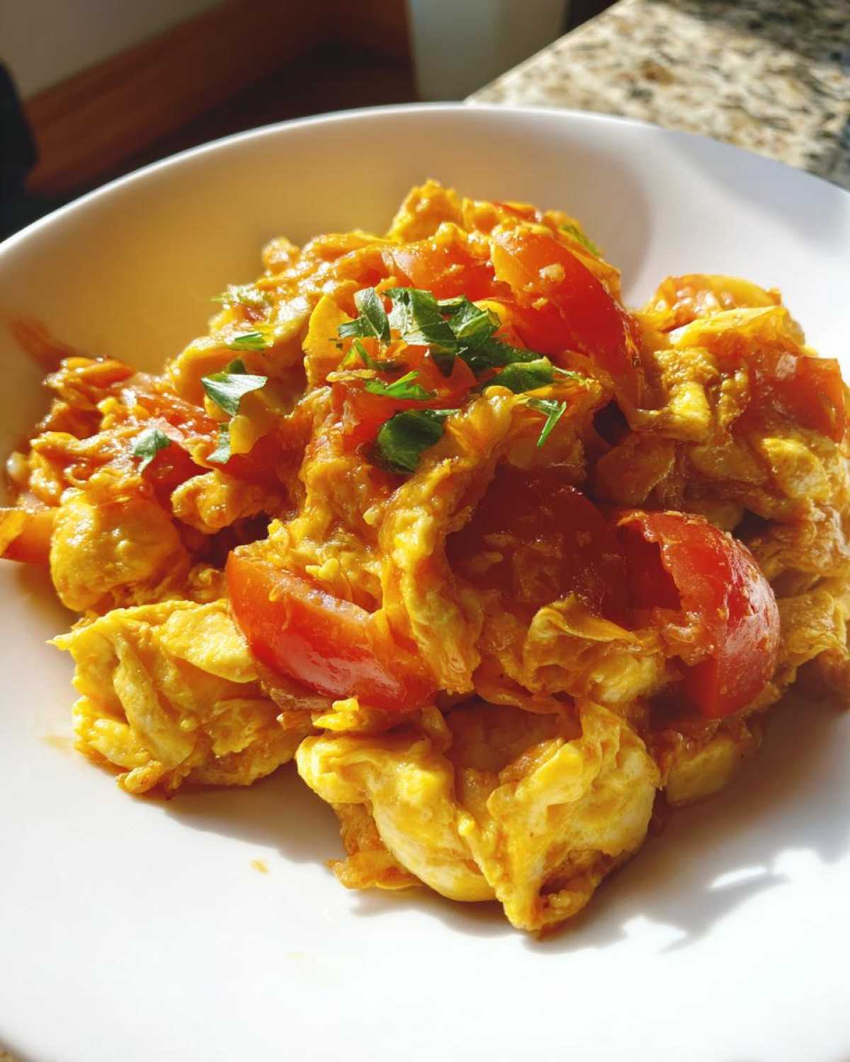 Close-up of vibrant Chinese Tomato Egg Stir-Fry with fluffy eggs and bright red tomatoes, garnished with green herbs.