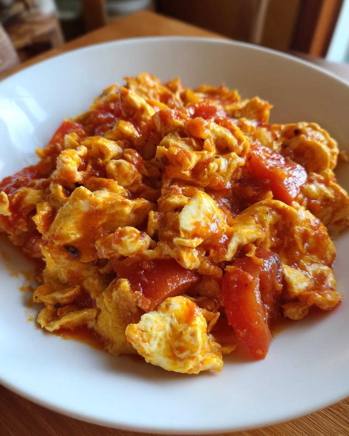 A close-up serving of vibrant Chinese Tomato Egg Stir-Fry with fluffy scrambled eggs and rich tomato sauce in a white bowl.