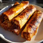 Close-up of golden brown, crispy Chipotle Chicken Taquitos Baked Crisp piled on a light-colored plate.
