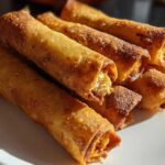 A pile of golden brown, crispy Chipotle Chicken Taquitos Baked Crisp stacked on a white plate.