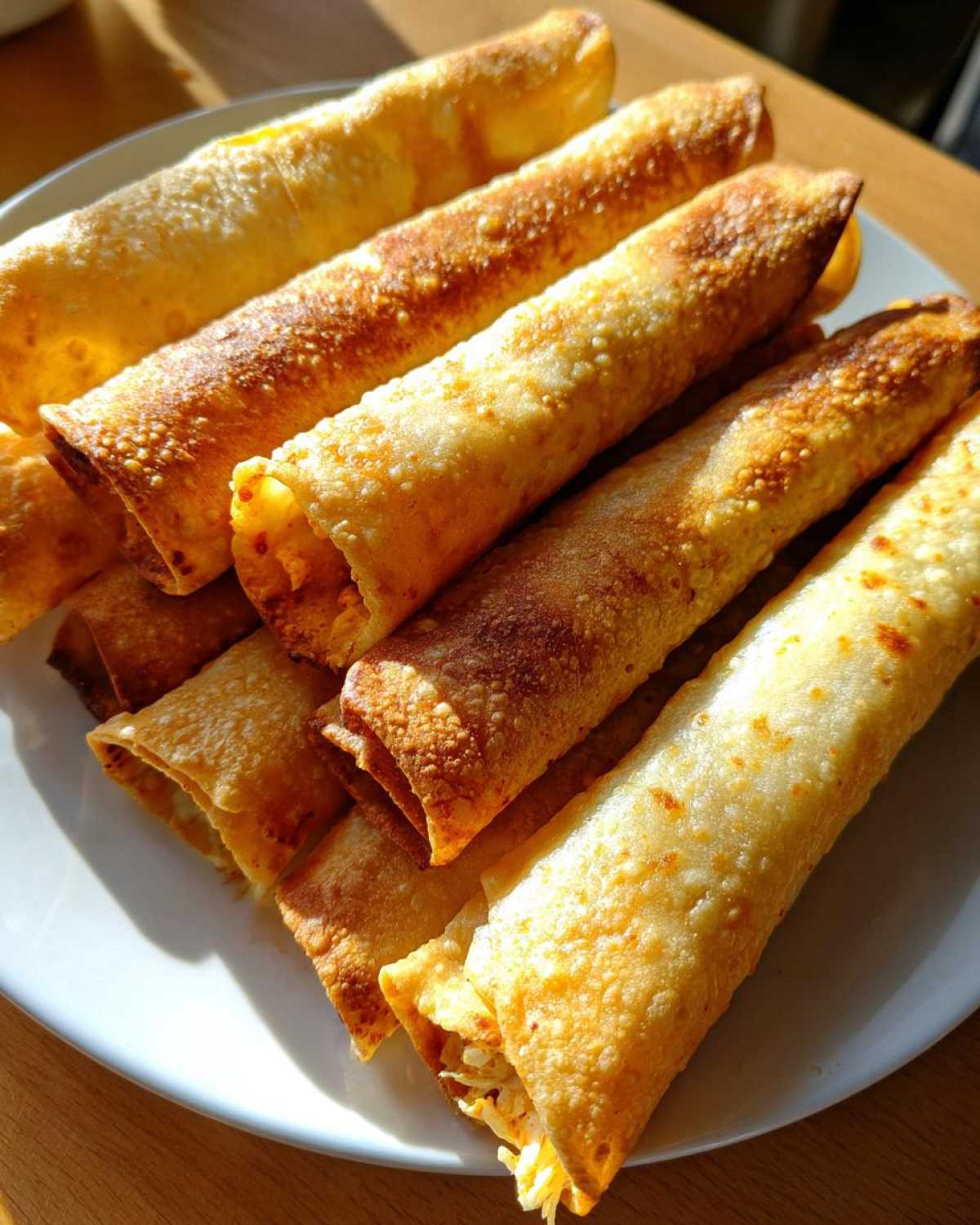 A plate piled high with golden, crispy baked Chipotle Chicken Taquitos, showing their rolled texture.