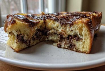 Close-up of Chocolate Chip Brioche Toast cut in half, showing melted chocolate chips inside and chocolate drizzle on top.