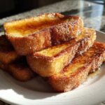 A stack of golden brown Churro French Toast Sticks coated in cinnamon sugar, resting on a white plate.