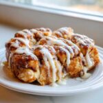 Close-up of warm Cinnamon Roll Pull-Apart Bread drizzled generously with white vanilla icing on a white plate.