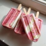 A close-up of several layered Coconut Strawberry Popsicles with Lime Zest sprinkled on top.
