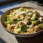 A close-up of a bowl filled with Cold Chicken Caesar Pasta Salad featuring rotini pasta, chicken chunks, romaine lettuce, and grated Parmesan.