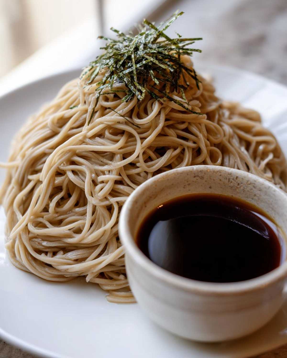 A serving of Cold Soba with Dipping Sauce, topped with shredded nori seaweed on a white plate.