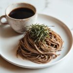 A neat mound of Cold Soba with Dipping Sauce, topped with shredded nori, served alongside a small cup of dark dipping sauce.