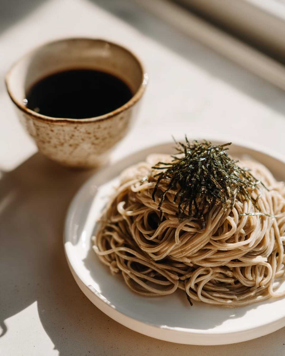 A serving of Cold Soba with Dipping Sauce, topped with shredded nori seaweed, served on a white plate.