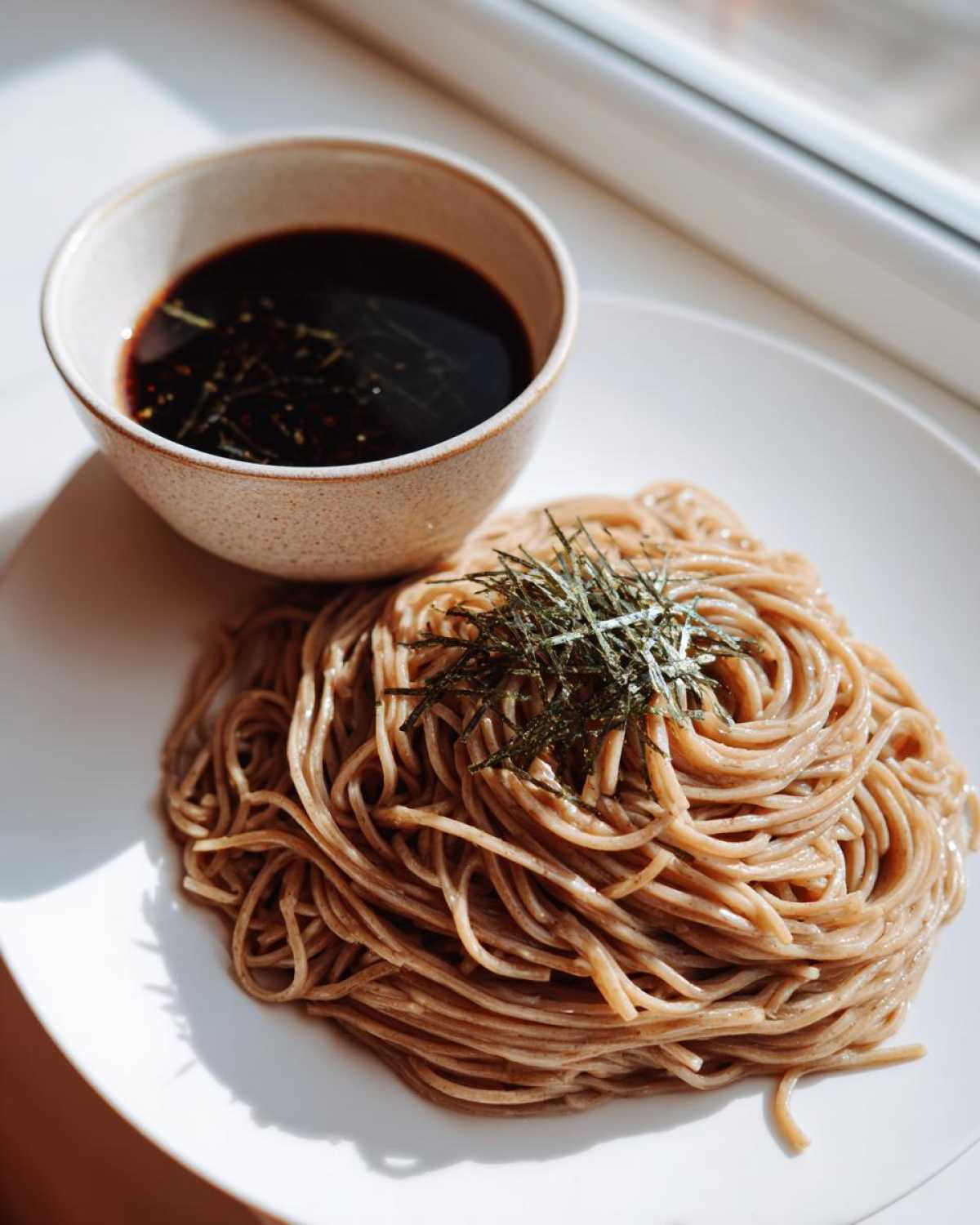 A serving of Cold Soba with Dipping Sauce, featuring chilled soba noodles topped with shredded nori next to a small bowl of dark sauce.