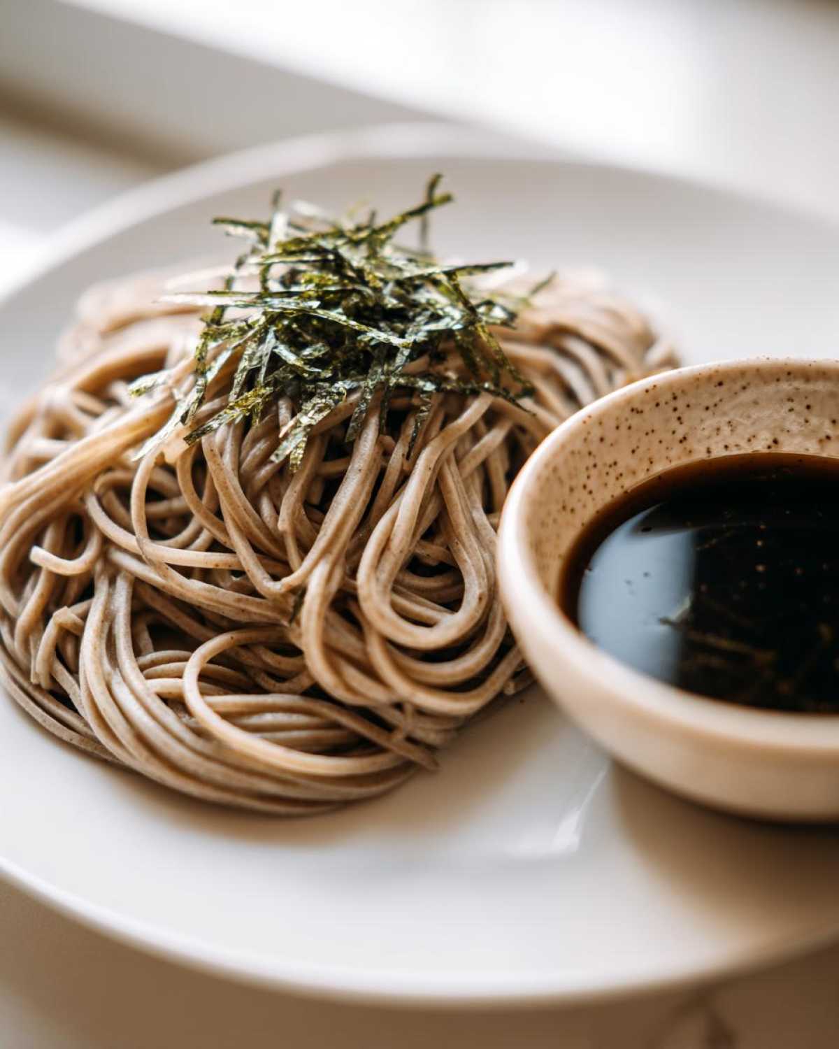 A serving of Cold Soba with Dipping Sauce, topped with shredded nori seaweed on a white plate.