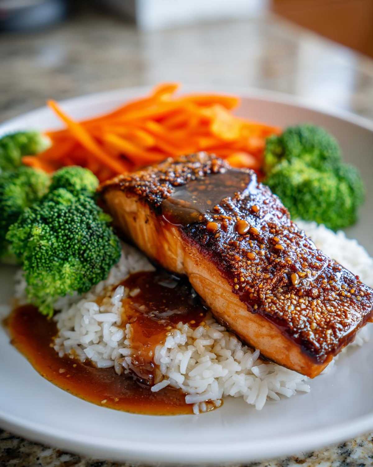 Close-up of a Crispy Salmon Rice Bowls serving featuring a glazed salmon fillet over white rice with broccoli and carrots.