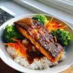 A close-up of a Crispy Salmon Rice Bowls featuring a perfectly seared salmon fillet over white rice with steamed broccoli and shredded carrots.