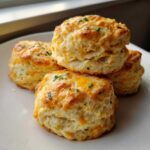 A stack of four golden, fluffy Chive Cheddar Biscuits topped with melted cheese and fresh chives.