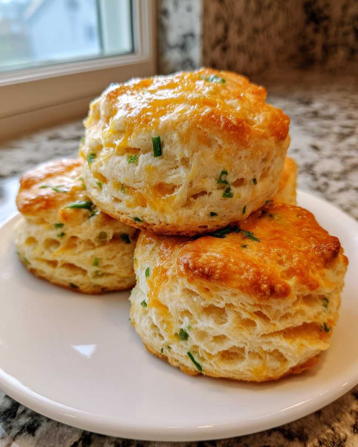A stack of four golden-brown, fluffy Chive Cheddar Biscuits with visible melted cheese and green chives.