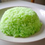 A perfectly molded mound of bright green Pandan Coconut Rice served on a white plate.