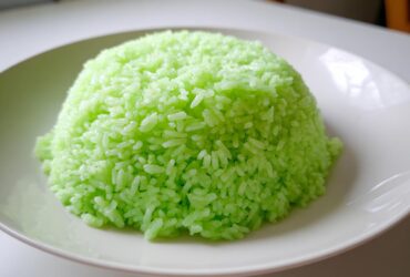 A perfectly molded mound of bright green Pandan Coconut Rice served on a white plate.