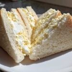 Two halves of a fluffy Tamago Sando Japanese Egg Sandwich, showing creamy egg salad filling between soft white bread.