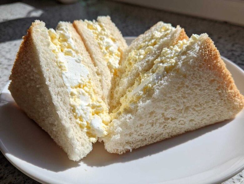 Two halves of a fluffy Tamago Sando Japanese Egg Sandwich, showing creamy egg salad filling between soft white bread.