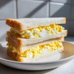 Two halves of a fluffy Tamago Sando Japanese Egg Sandwich stacked on a white plate.