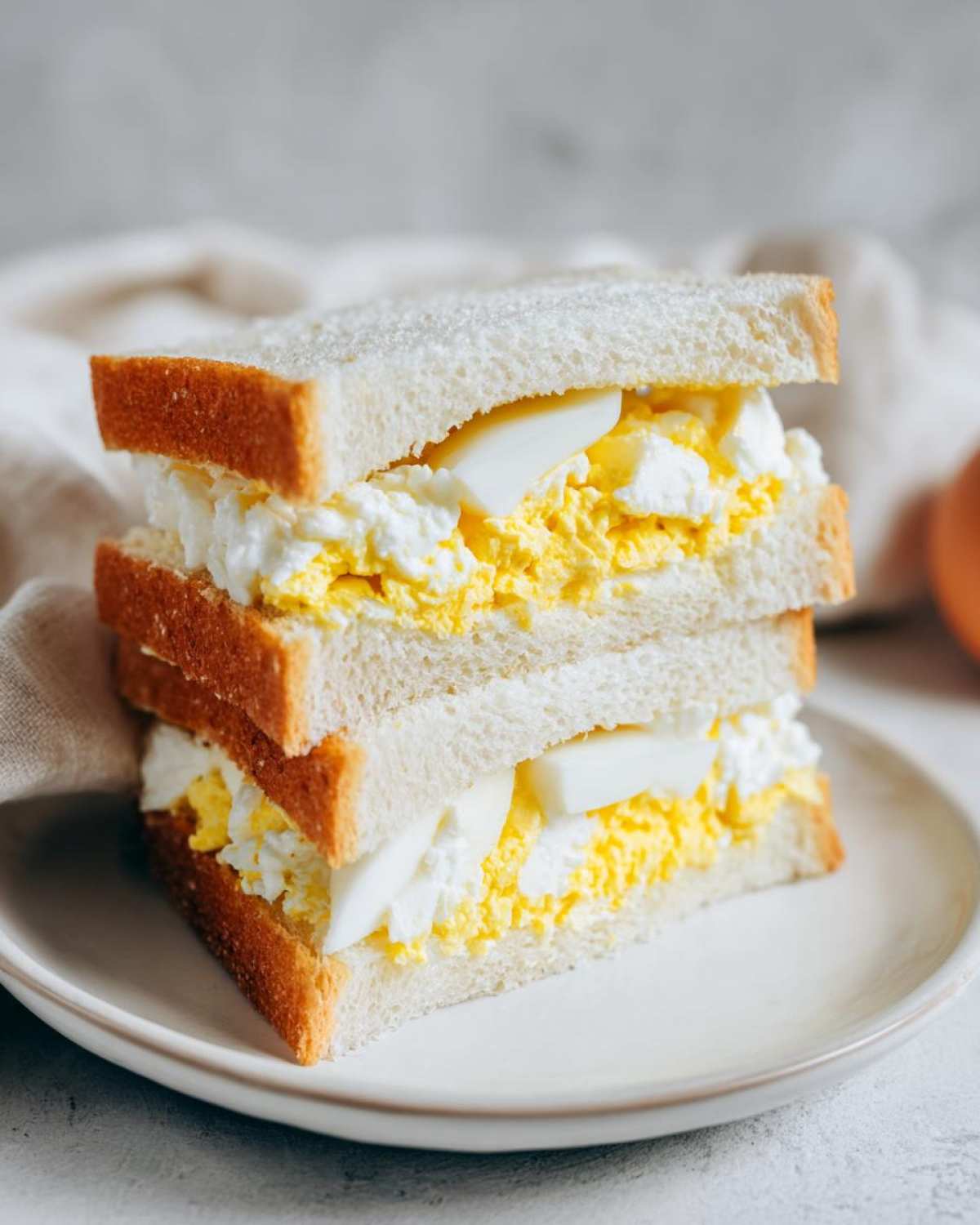 Two halves of a fluffy Tamago Sando Japanese Egg Sandwich stacked on a white plate.