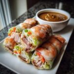 A stack of beautifully wrapped Fresh Spring Rolls with Peanut Sauce, featuring shrimp, lettuce, and vermicelli, served next to a dipping bowl.