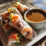 A plate of vibrant Fresh Spring Rolls with Peanut Sauce, showing shrimp and colorful vegetables wrapped in rice paper.