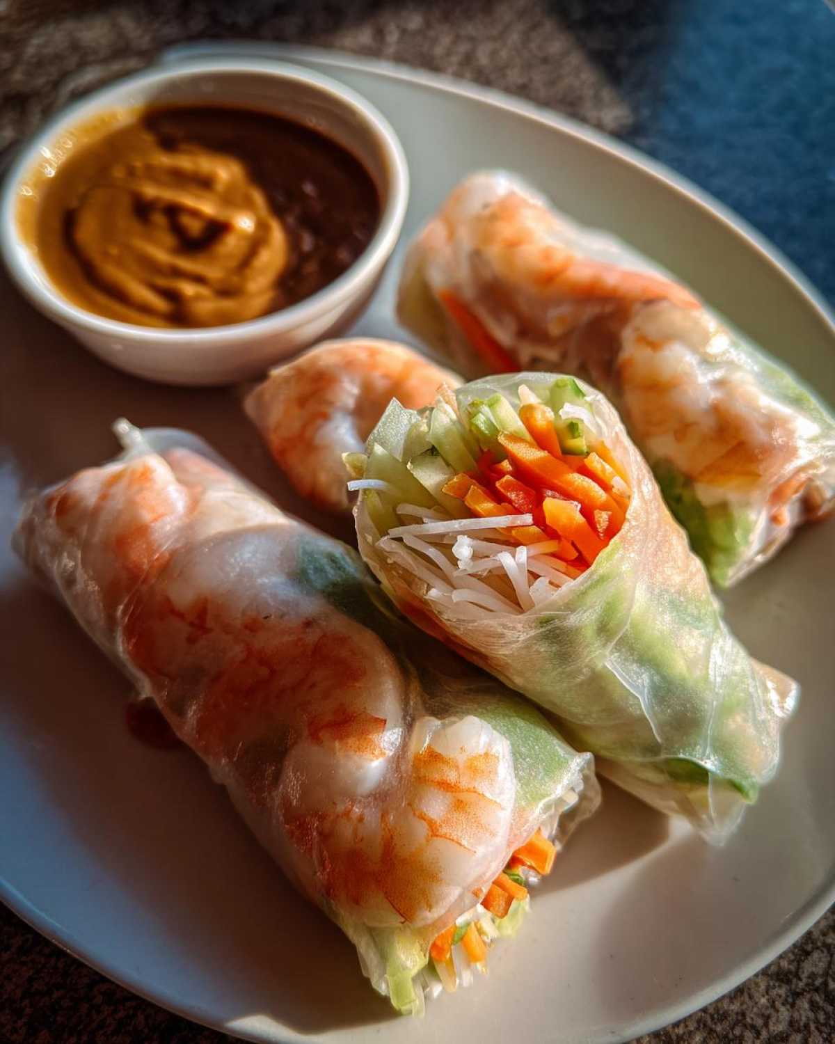 Three shrimp Fresh Spring Rolls with Peanut Sauce served on a light plate.