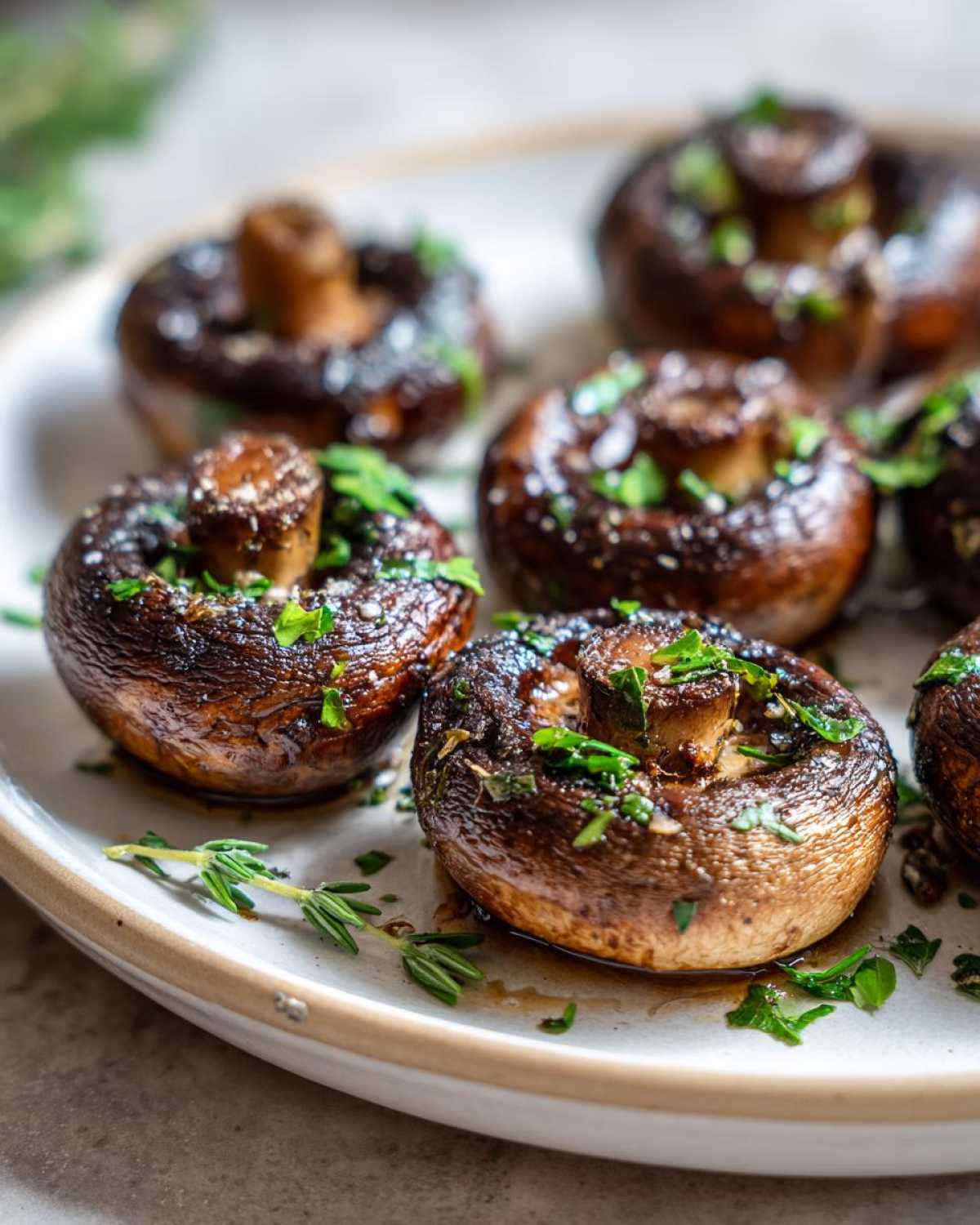 Close-up of sautéed Garlic Butter Mushrooms with Thyme, garnished with fresh parsley and sitting in butter sauce.