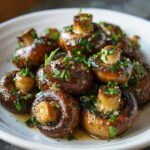 Close-up of perfectly cooked Garlic Butter Mushrooms with Thyme, glistening in sauce and topped with fresh herbs.