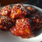A plate piled high with sticky, glazed Gochujang Honey Chicken Thighs, sprinkled generously with white sesame seeds.