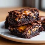 Close-up of two stacked, fudgy Dulce de Leche Brownie Bars oozing with caramel filling on a white plate.