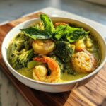 A vibrant bowl of Green Curry Shrimp with Coconut Milk, featuring large shrimp and broccoli florets, garnished with fresh basil.
