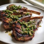 Close-up of perfectly seared Grilled Lamb Chops with Mint Gremolata piled high on a white plate.