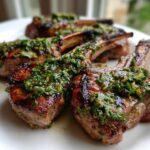 Close-up of perfectly grilled lamb chops topped generously with bright green mint gremolata sauce.