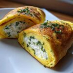 Two halves of a golden Herb Goat Cheese Omelet Roll filled with creamy white cheese and green herbs, garnished with chives.