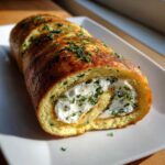 Close-up of a sliced Herb Goat Cheese Omelet Roll filled with creamy white cheese and green herbs, resting on a white platter.