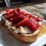 A close-up view of Honey Strawberry Ricotta Toast on a white plate, drizzled with honey.