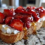 A close-up of Honey Strawberry Ricotta Toast featuring thick ricotta, sliced strawberries, and honey drizzling down the side.