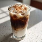 A tall glass of Horchata Iced Coffee Refresher layered with milk, dark coffee, ice, and topped with cinnamon.