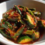 Close-up of vibrant Korean Cucumber Salad Oi Muchim, featuring bright green cucumber chunks coated in spicy red chili flakes and sesame seeds.