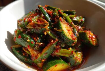 Close-up of vibrant Korean Cucumber Salad Oi Muchim, featuring bright green cucumber chunks coated in spicy red chili flakes and sesame seeds.