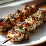 Close-up of juicy Lemon Herb Grilled Chicken Skewers, showing char marks and green herbs on a white plate.