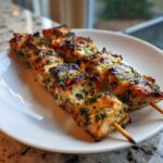 Two skewers of juicy Lemon Herb Grilled Chicken Skewers, beautifully charred and topped with green herbs, served on a white plate.