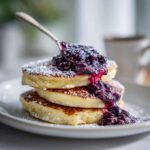 Stack of three fluffy Lemon Ricotta Pancakes dusted with powdered sugar and topped with rich blueberry compote.