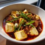 Close-up of vibrant Mapo Tofu with Ground Pork, featuring silken tofu cubes in chili oil sauce, topped with ground meat and green onions.